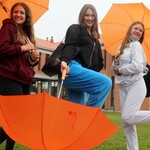 Trzy uśmiechnięte dziewczyny z pomarańczowymi parasolkami.