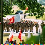 Żołnierze Wojska Polskiego ustawieni na placu. Widoczne powiewające biało-czerwone flagi