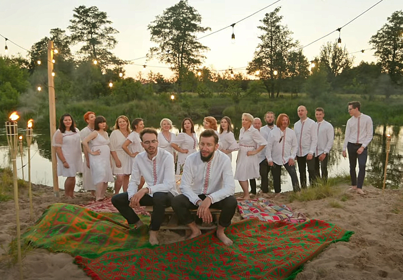 Grupa muzyków w białych koszulach na łonie przyrody.