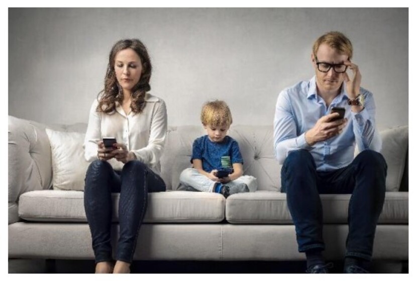 Dwoje dorosłych i dziecko siedzą na kanapie i patrzą się w telefony.