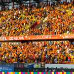 Na trybunach siedzą kibice Jagiellonii Białystok ubrani w żółto-czerwone barwy