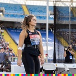 Kobieta w sportowym stroju stojąca na tle trybun oraz siatki
