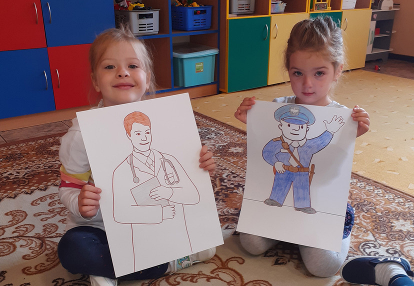 Dwie dziewczynki w przedszkolu prezentują rysunki.