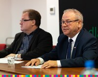 Marek Olbryś wraz z innym mężczyzną siedzi przy stole podczas konferencji