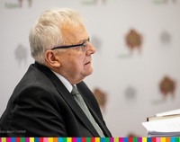 Bogusław Dębski, przewodniczący sejmiku, siedzący profilem na tle promocyjnej ścianki województwa