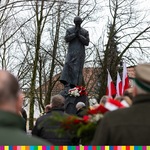Zdjęcie osób odwróconych plecami. W oddali widać pomnik bł. księdza Jerzego Popiełuszki oraz flag biało-czerwone