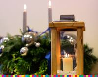 Lampion z płonącą świecą na tle stroika świątecznego.