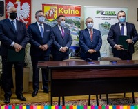 Pięciu mężczyzn, przed nimi stoi stół, za nimi widać herb Polski oraz herb miasta Kolno
