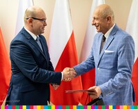 Marszałek Artur Kosicki podaje dłoń Sylwestrowi Zawadzkiemu, ustępującemu przewodniczącemu WRDS na tle biało-czerwonych flag