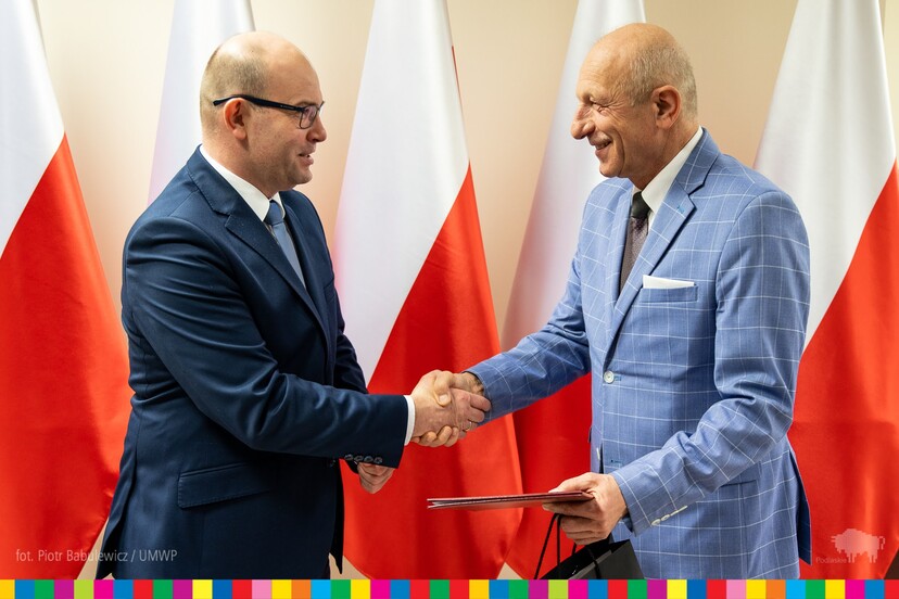 Marszałek Artur Kosicki podaje dłoń Sylwestrowi Zawadzkiemu, ustępującemu przewodniczącemu WRDS na tle biało-czerwonych flag