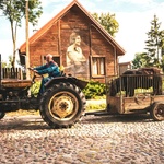 Kobieta na traktorze. W tle chata z drewnalem.