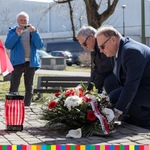 Prof. Krzysztof Sychowicz sklada wieńce przed pomnikiem w towarzystwie drugiej osoby. W oddali widać fotografa robiącego zdjęcie
