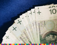 Banknoty o nominale 100 zł z profilem Władysława Jagiełły leżą na niebieskiej powierzchni ułożone w wachlarz