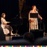 Dwie kobiety na scenie, jedna z nich śpiewa przed mikrofonem, druga gra na pianinie 