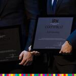 Zbliżenie na sylwetki dwóch mężczyzn, trzymających w rękach certyfikaty 
