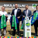 Wicemarszałek Łukaszewicz i trzej mężczyźni stoją z szalikami w ręku na tle MKS Mielnik