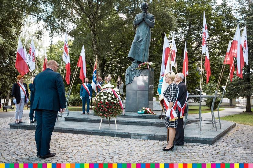 Pomnik ks. Popiełuszko. Przy nim flagi, kwiaty i ludzie.