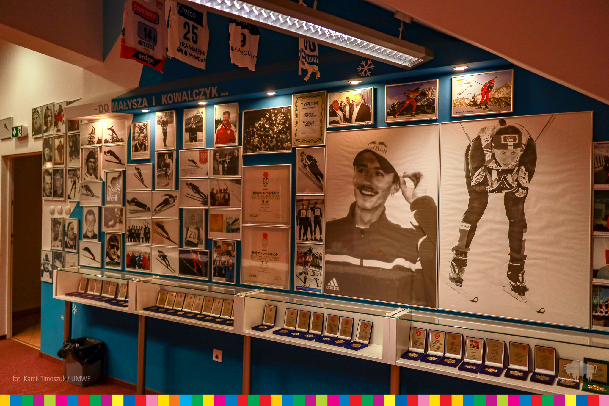 Ściana ze zdjęciami poslkich sportowców oraz leżące pod nią medale olimpijskie