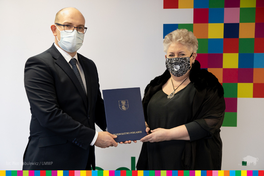 Marszałek Artur Kosicki i prof. Violetta Bielecka wspólnie trzymają teczkę z nominacją, pozując do zdjęcia.